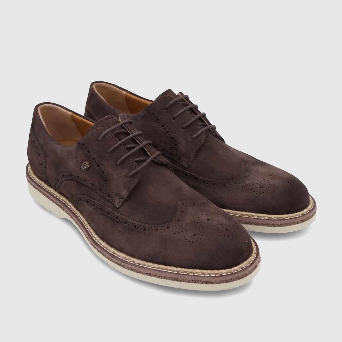 A pair of men's Crockett and Jones brown suede lace-up brogues with wingtip detailing and white soles, angled on a white