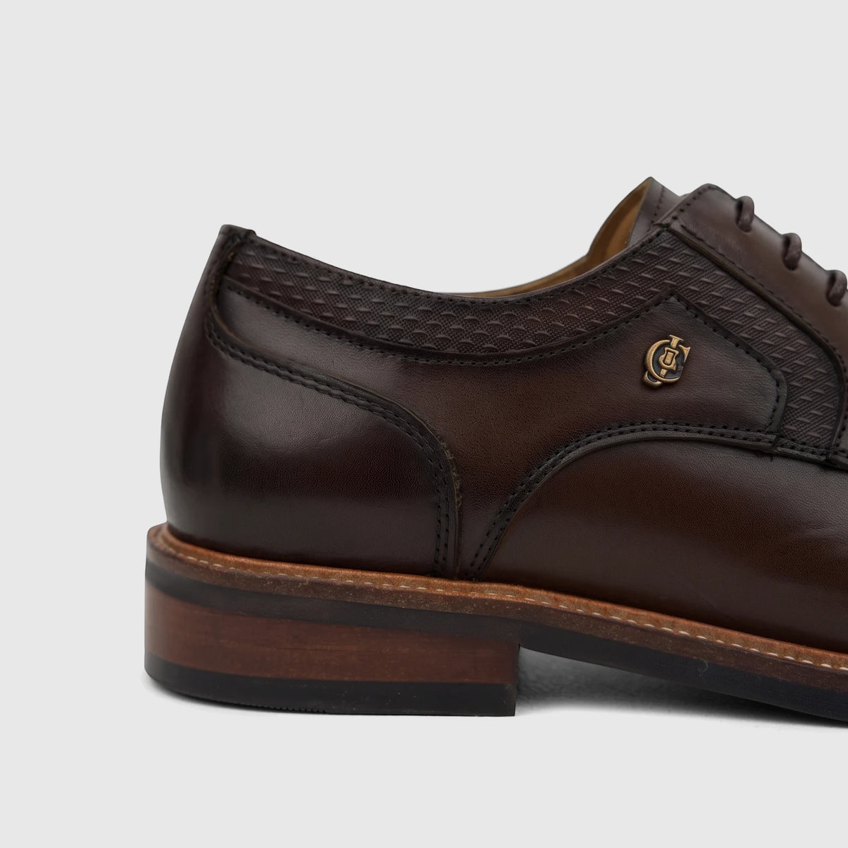 Close-up of a Crockett And Jones Men's Guilio coffee brown leather lace-up shoe with intricate stitching and gold emblem.