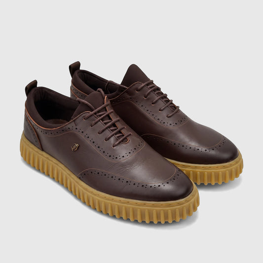 Brown leather men's lace-up shoe with brogue details and a chunky tan ribbed sole, viewed from the side.
