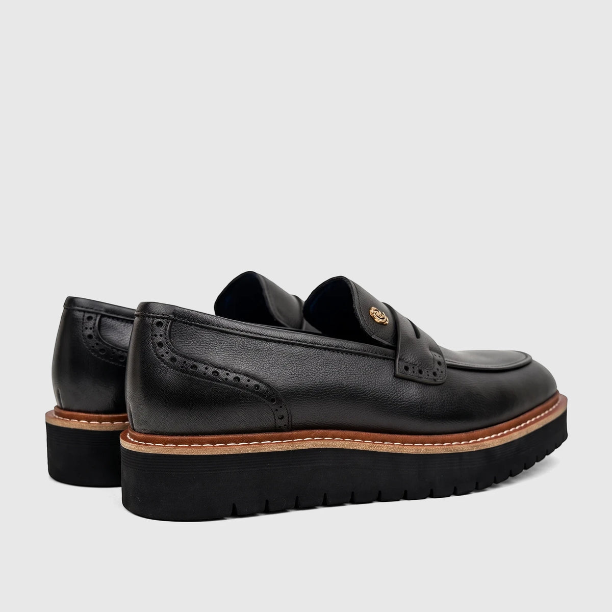 Pair of men's black leather chunky sole loafers from Crockett And Jones, featuring brogue details and a gold emblem, viewed