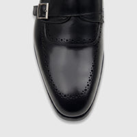 Close-up of a men's black leather double monk strap dress shoe with brogue detailing and a silver buckle.