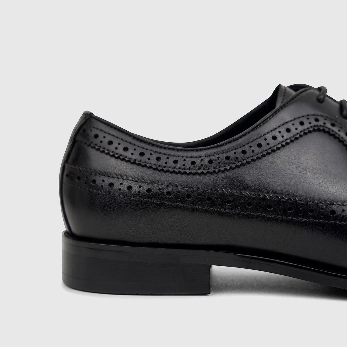Close-up side view of a men's black leather lace-up brogue dress shoe with perforated detailing and a sturdy heel.