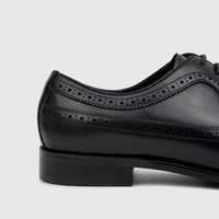 Close-up side view of a men's black leather lace-up brogue dress shoe with perforated detailing and a sturdy heel.