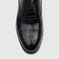 Overhead view of a glossy Fabino Men's black leather lace-up dress shoe with intricate brogue detailing on the cap toe.