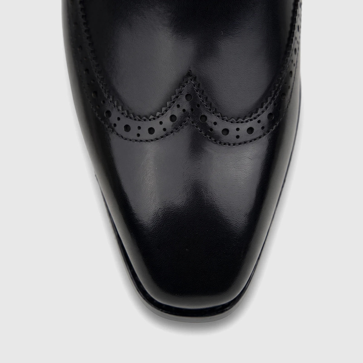 Close-up of a black leather men's lace-up brogue dress shoe from Fabino, showcasing the detailed perforations and shiny