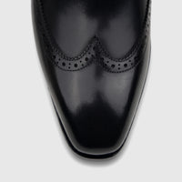 Close-up of a black leather men's lace-up brogue dress shoe from Fabino, showcasing the detailed perforations and shiny