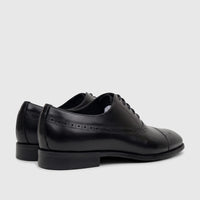 A pair of men's black leather lace-up dress shoes with brogue detailing, viewed from a rear side angle.