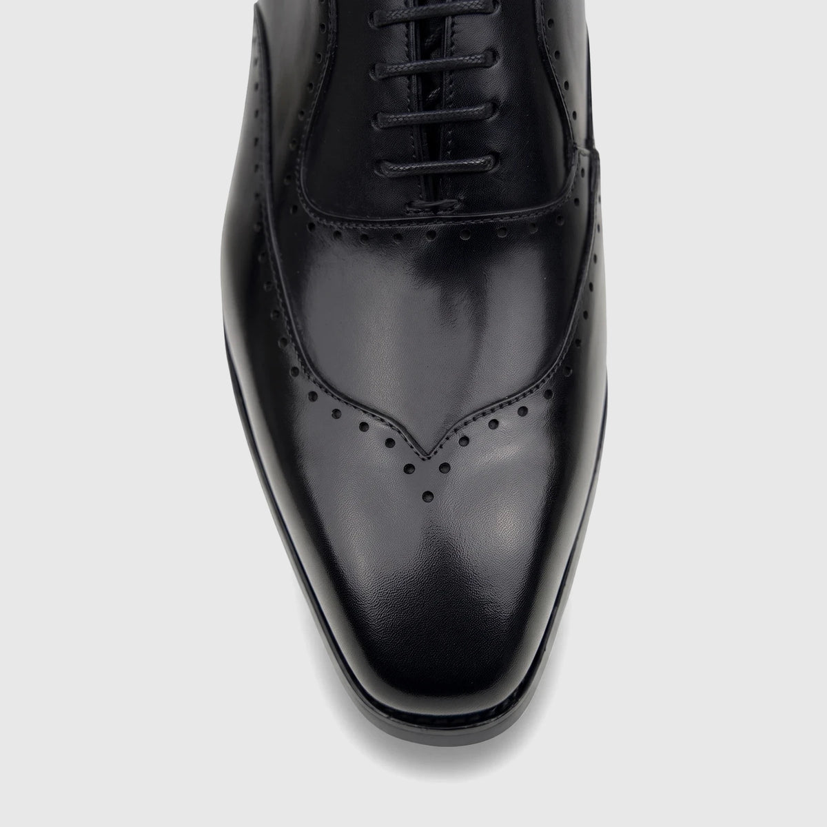 Close-up top view of a men's black leather lace-up dress shoe with brogue details, glossy finish, and sleek toe.