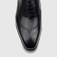 Close-up top view of a men's black leather lace-up dress shoe with brogue details, glossy finish, and sleek toe.