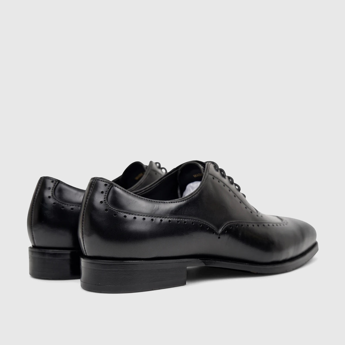 Black leather lace-up men's dress shoes, featuring classic brogue detailing and a polished finish, seen from a slight