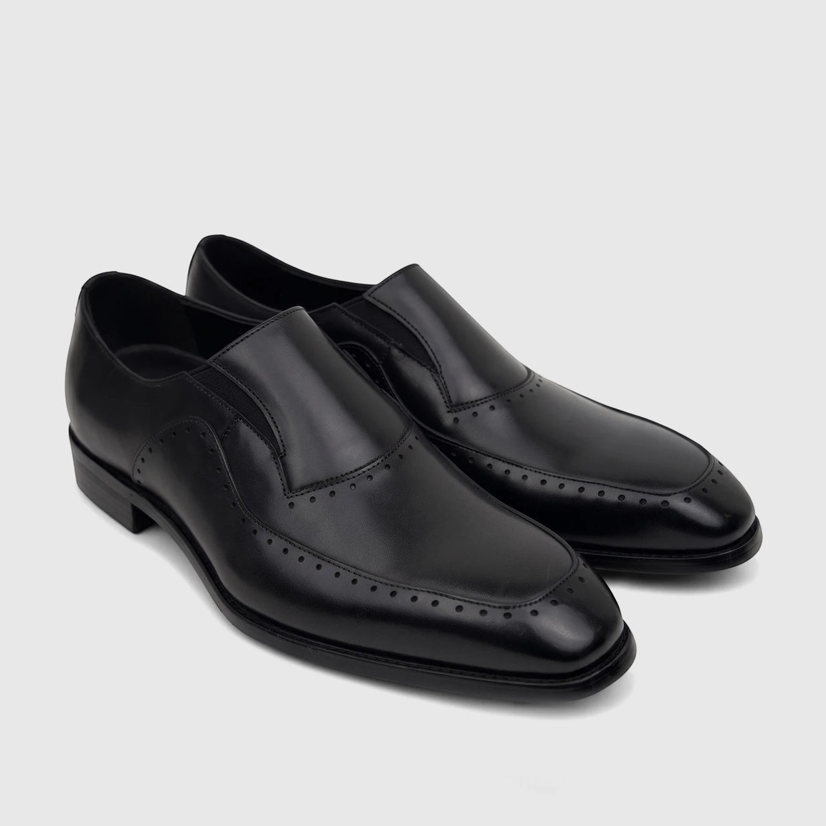 Black leather men's slip-on dress shoes, featuring brogue detailing and a polished finish, displayed on a clean surface.