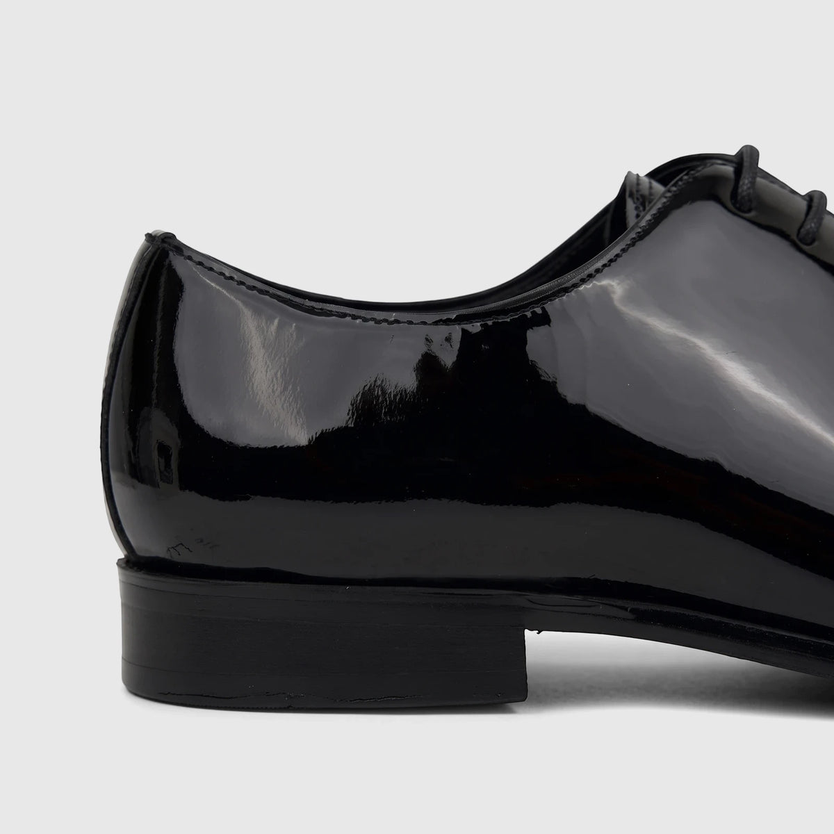 Close-up side view of a glossy black patent leather men's dress lace-up shoe, showcasing its sleek design.