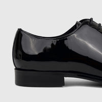 Close-up side view of a glossy black patent leather men's dress lace-up shoe, showcasing its sleek design.
