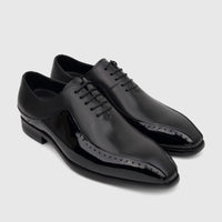 A pair of men's black patent leather lace-up oxford dress shoes with brogue detailing, viewed from a slight high angle.
