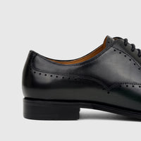 Close-up side view of a Fabino Men's green leather lace-up dress shoe with brogue details, on a white background.
