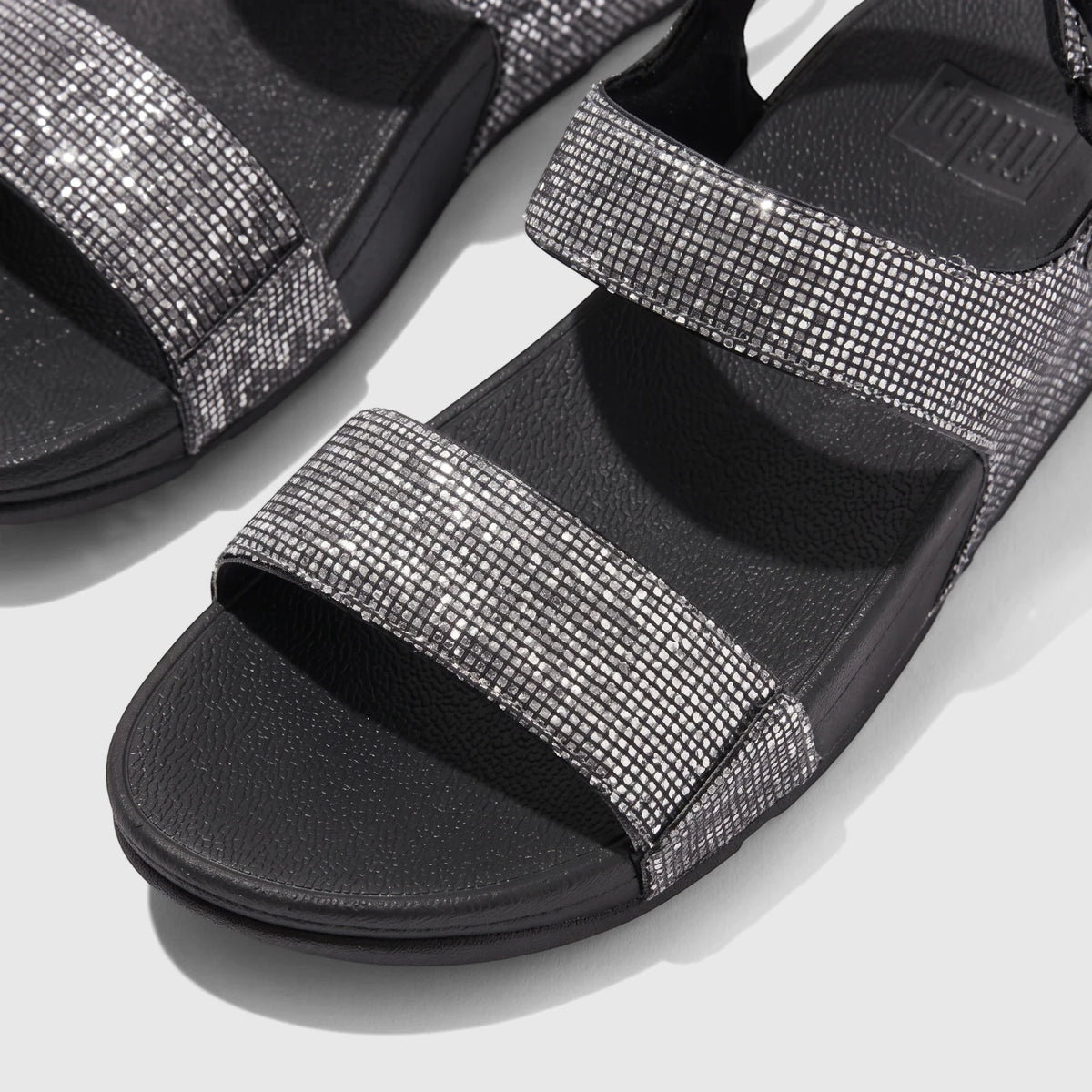Close-up of a pair of Fit Flop Ladies Comfort Sandal Lulu Glitterball Back Strap in silver with black soles, showcasing the
