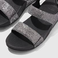 Close-up of a pair of Fit Flop Ladies Comfort Sandal Lulu Glitterball Back Strap in silver with black soles, showcasing the