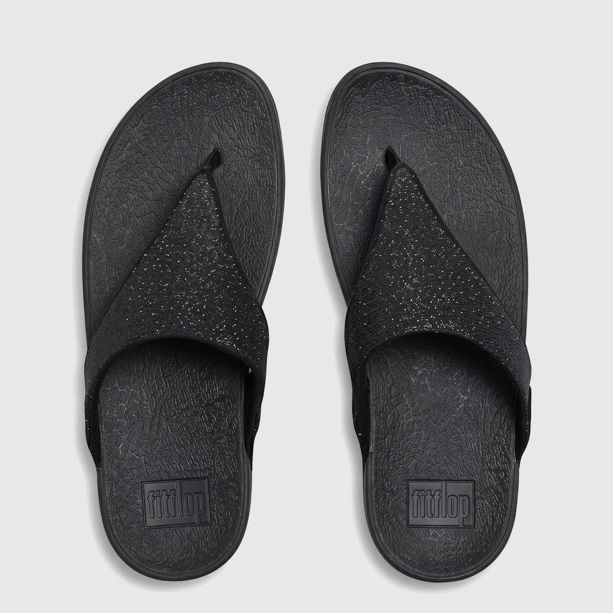 A pair of black Fit Flop Lulu Shimmerglitz comfort sandals, presented in a flat-lay view on a white background.