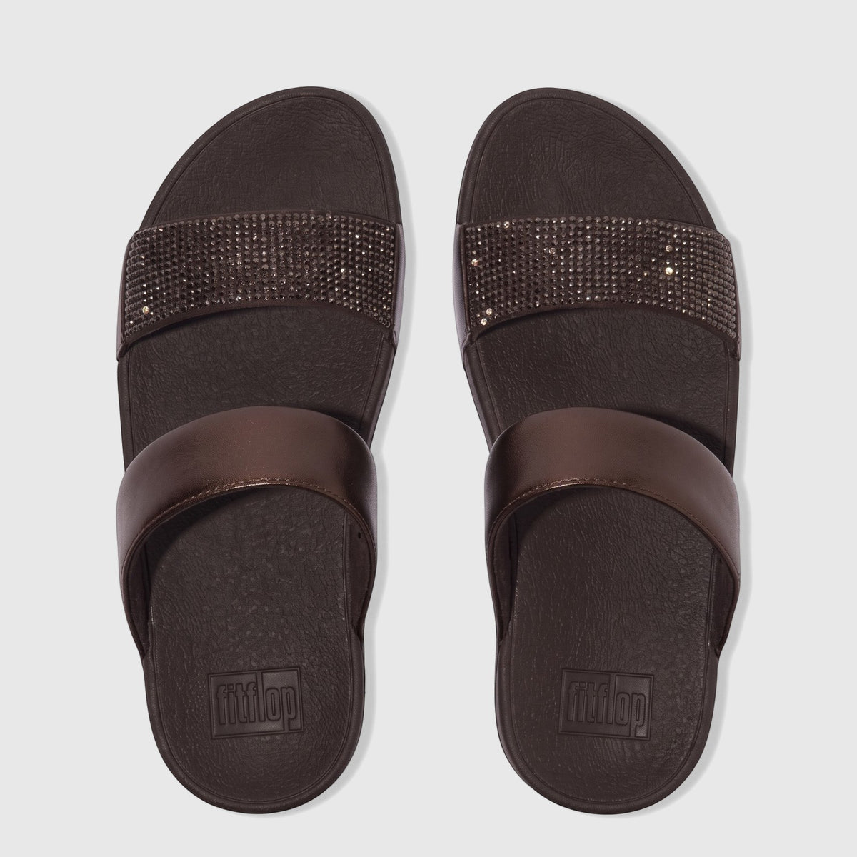 Pair of chocolate brown Fit Flop Lulu Crystal Embellished Slide sandals, featuring one plain and one crystal-studded strap,