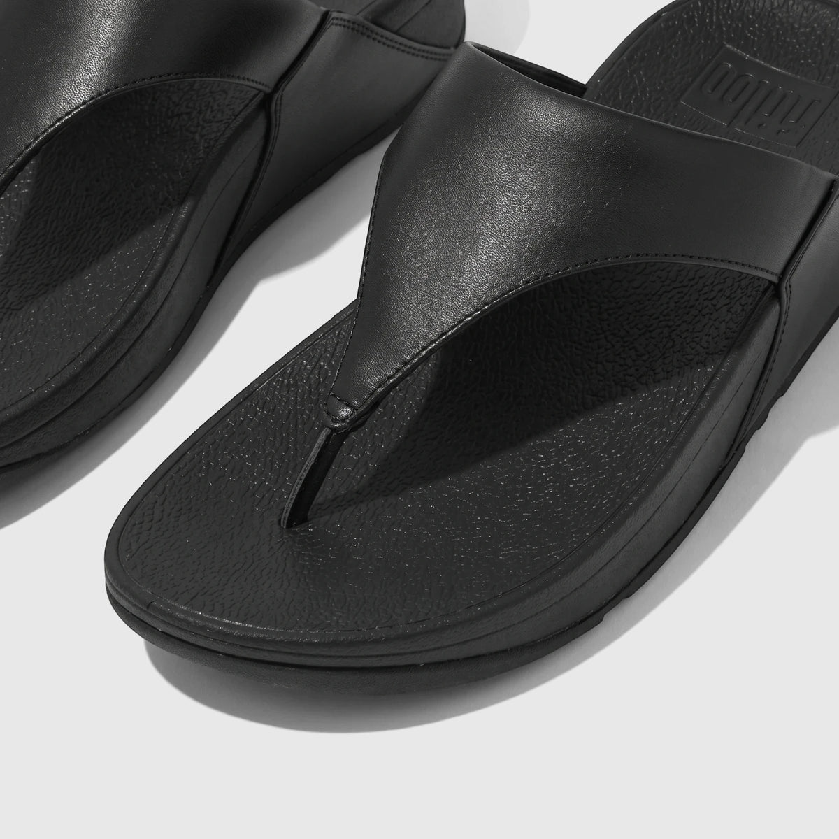 A close-up view of black Fit Flop Lulu leather comfort sandals, featuring a thong-style strap and a platform sole.