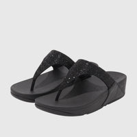 A pair of black FitFlop Lulu Crystal Embellished comfort thong sandals, featuring sparkling straps and a platform sole, on a