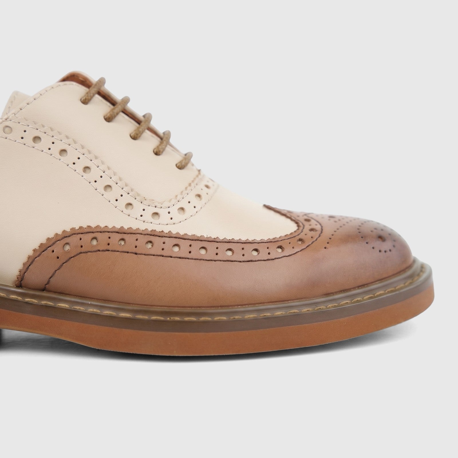 Close-up of a women's formal two-tone brown and cream leather full brogue wingtip lace-up shoe.