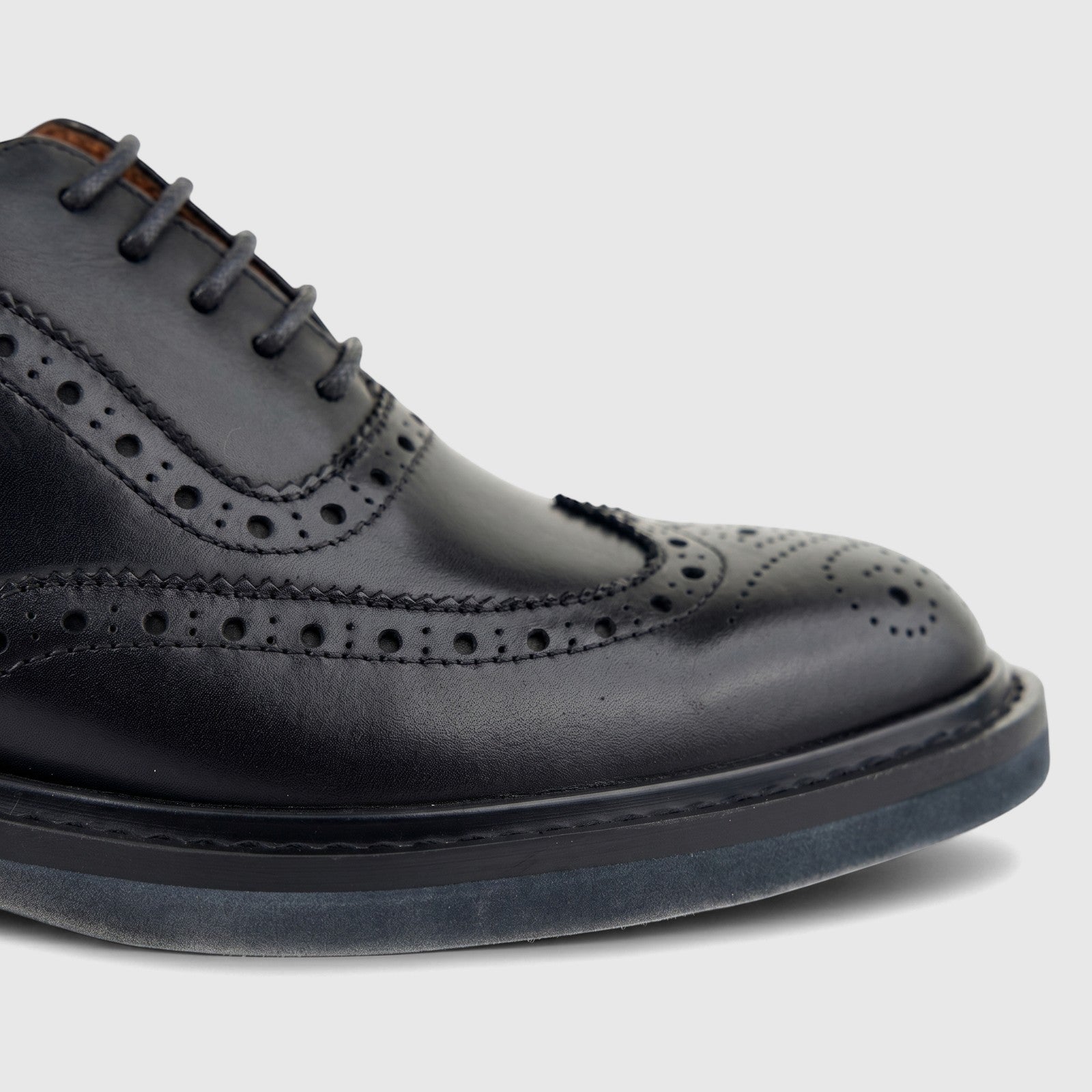 Close-up of a black leather full brogue wingtip lace-up shoe with intricate perforations and lacing details.