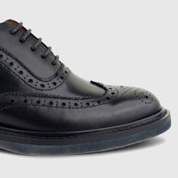 Close-up of a black leather full brogue wingtip lace-up shoe with intricate perforations and lacing details.