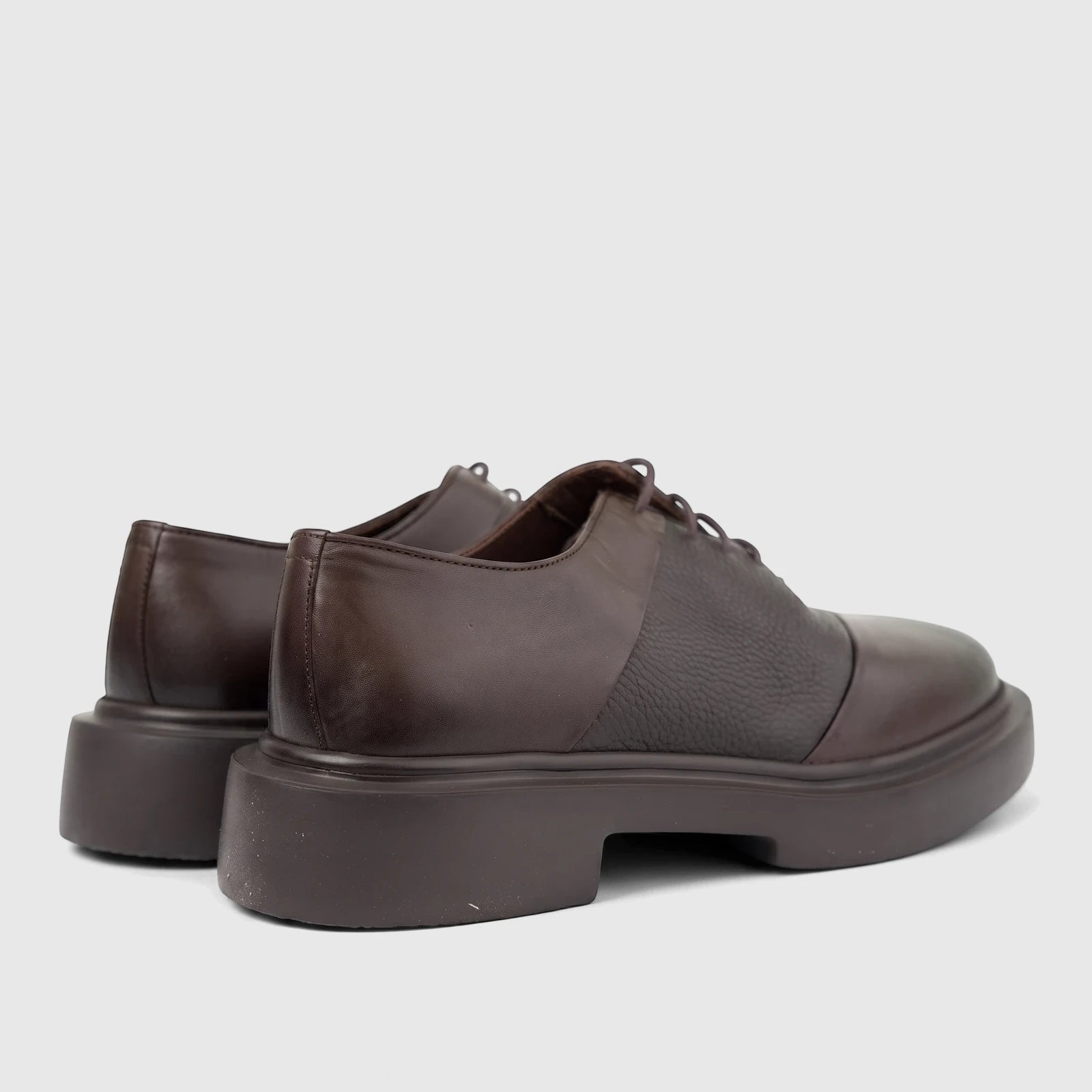Dark brown leather chunky sole lace-up oxford shoes with smooth and textured panels, shown from a low rear-side angle.