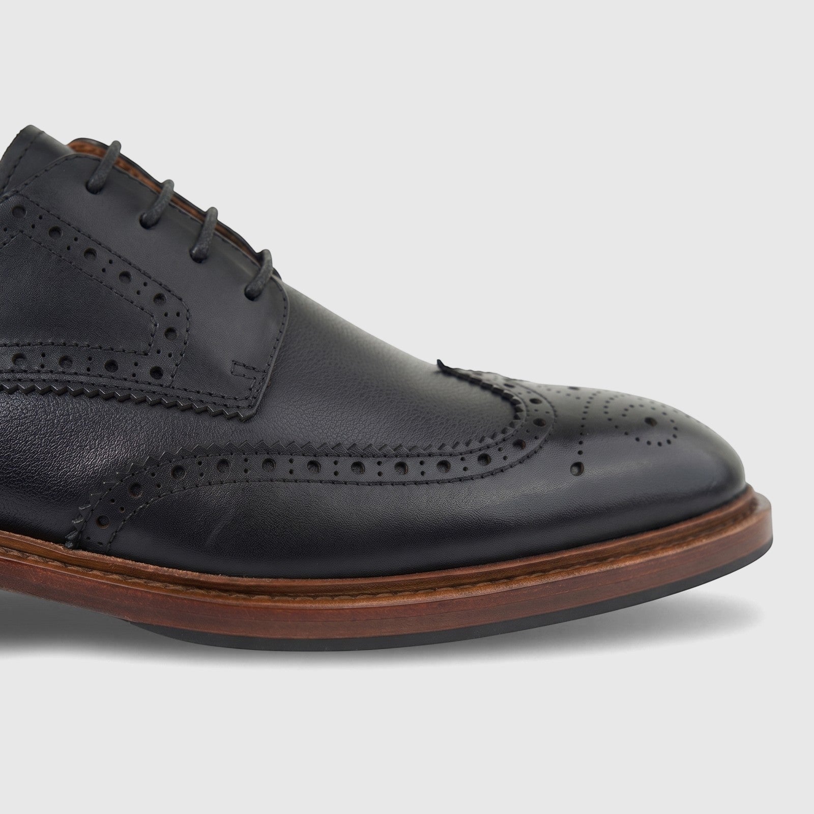 Close-up of a black leather men's formal brogue shoe with lace-up closure and a brown sole against a white background.