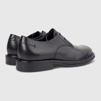 A pair of black leather men's derby shoes with a chunky sole, viewed from a rear-quarter angle on a white background.