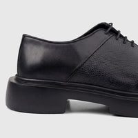 Close-up profile view of a Formales men's black leather chunky sole lace-up shoe with textured and smooth panels.