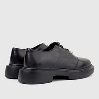 A pair of men's black leather lace-up shoes with chunky soles, viewed from the back-right showing the textured upper.