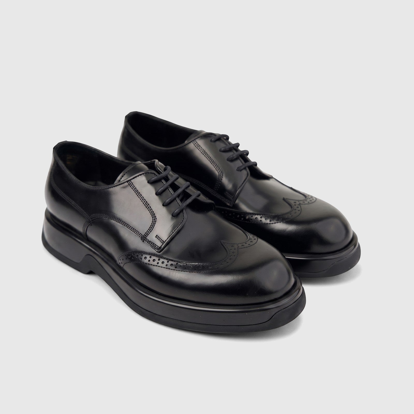 A pair of black hi-shine formal leather lace-up shoes for men with chunky soles and wingtip broguing.