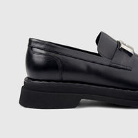 Close-up side view of a Formales Men's black leather chunky sole slip-on loafer with a silver buckle detail.