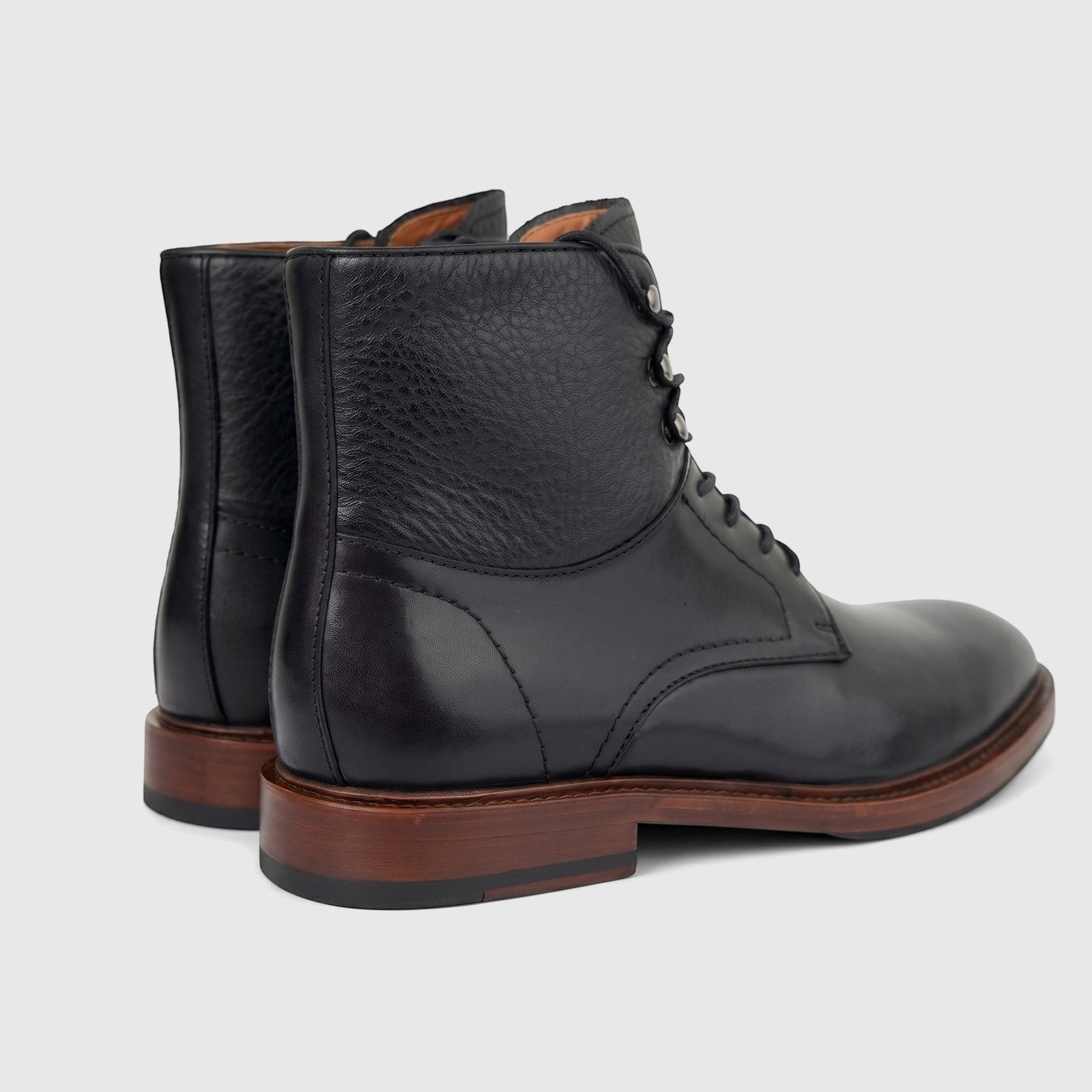 A pair of men's black leather lace-up boots with pebbled and polished textures, brown soles, and black heels, viewed from