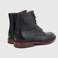 A pair of men's black leather lace-up boots with pebbled and polished textures, brown soles, and black heels, viewed from