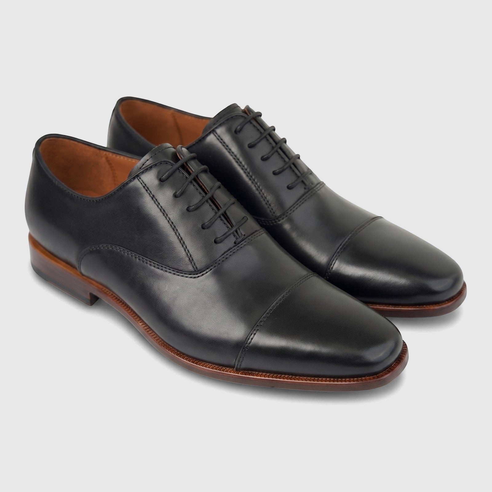A pair of Formales Men's black leather lace-up cap toe dress shoes with brown soles, captured at a slight angle.