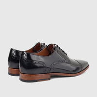 Formales men's black leather lace-up dress shoes, featuring brogue details and brown stacked heels, captured in a rear-side