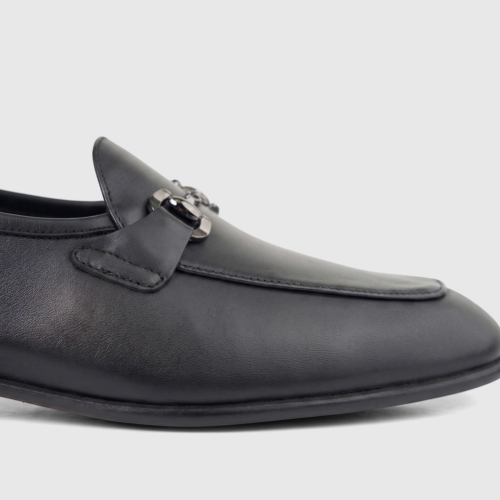 Close-up of a black leather men's loafer with a silver-toned chain-link hardware detail on the vamp, photographed from the