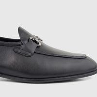 Close-up of a black leather men's loafer with a silver-toned chain-link hardware detail on the vamp, photographed from the