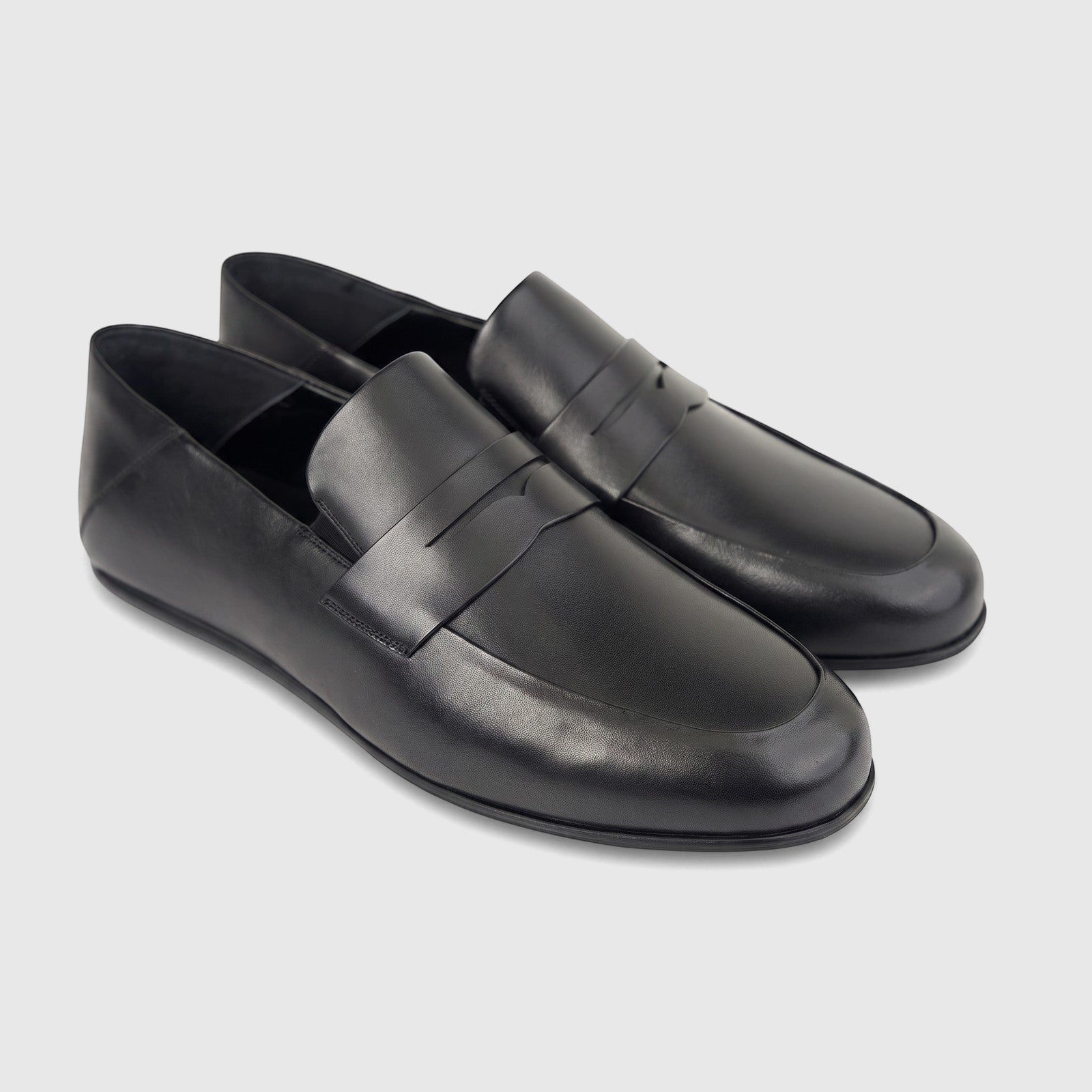 A pair of elegant black leather men's slip-on loafers, seen from a slightly elevated front-side angle on a white background.