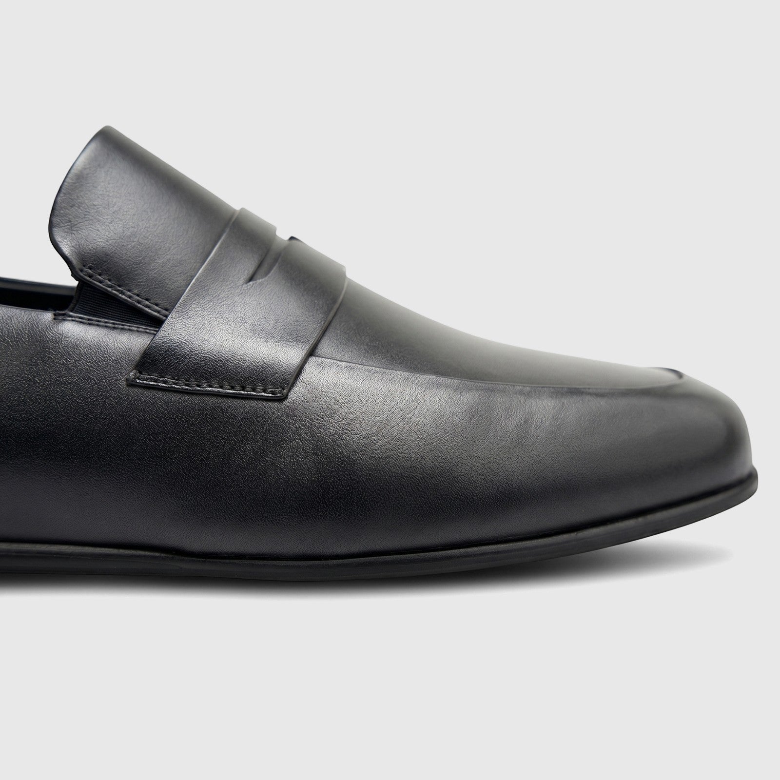 Close-up side view of a Formales men's black leather slip-on shoe, featuring smooth leather and a penny loafer strap.