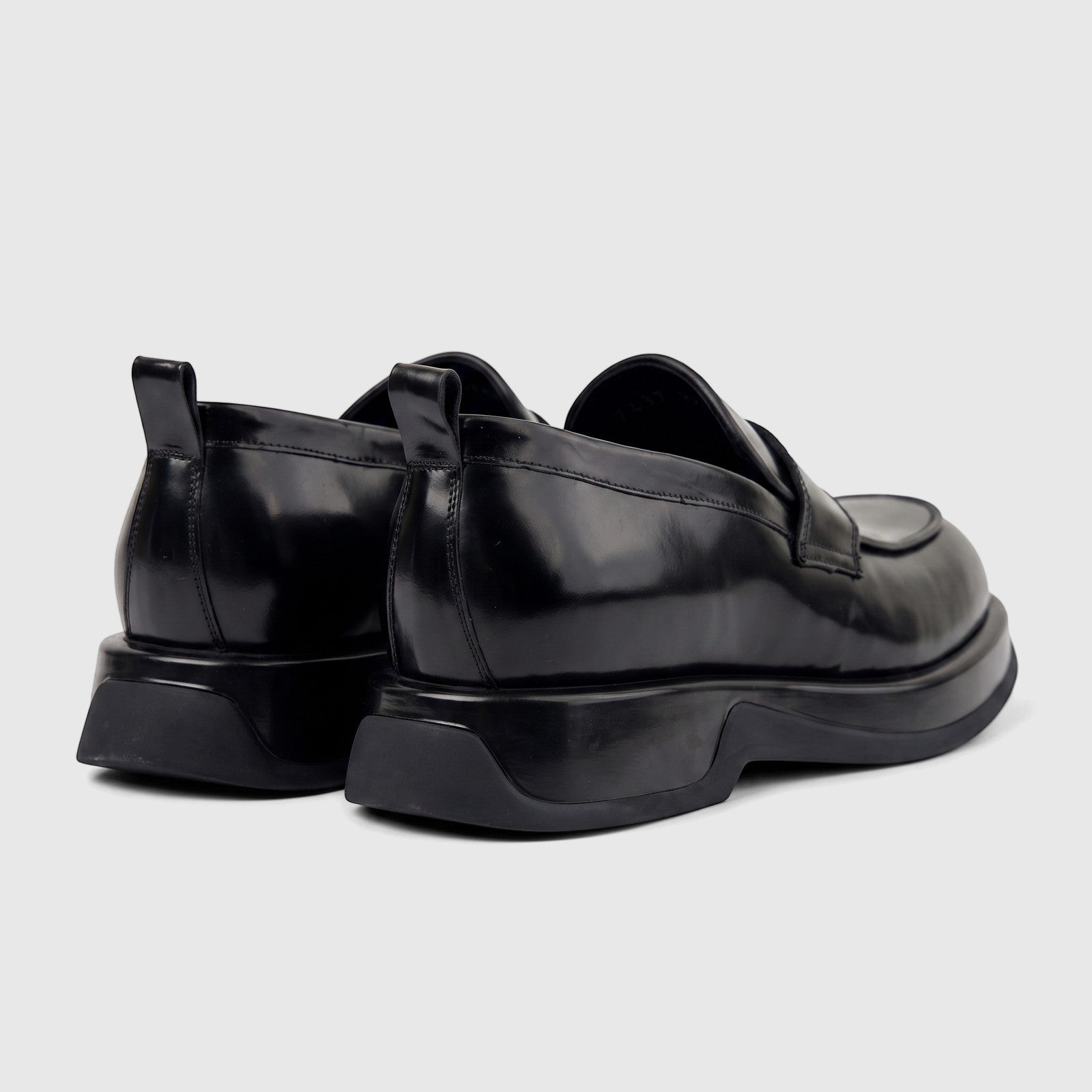 Black patent leather chunky sole loafers for men, featuring pull tabs at the heel, shown from a rear-side view.