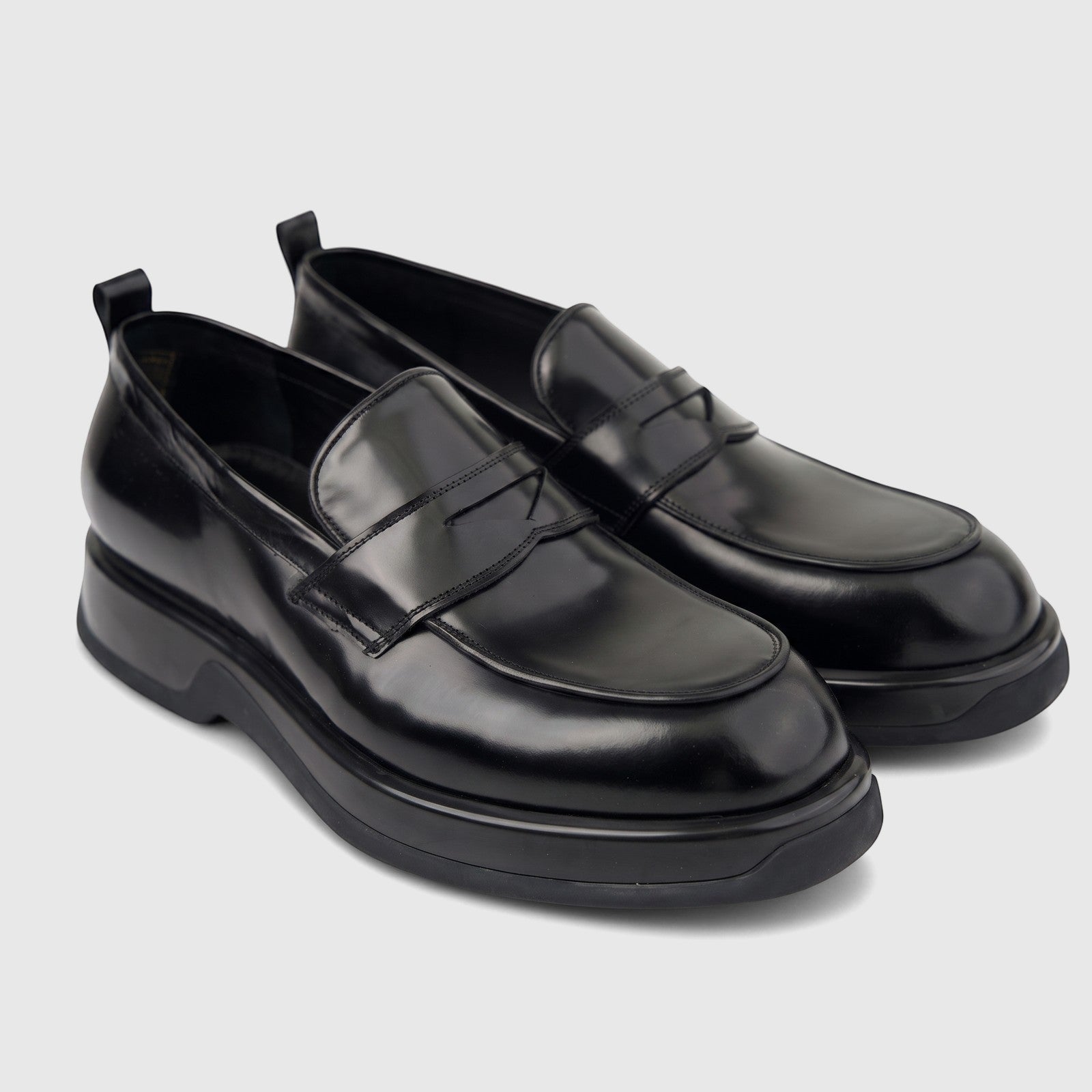 Black patent leather men's loafers with chunky soles, viewed from a slight angle. Formal yet modern footwear.