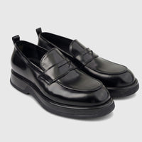 Black patent leather men's loafers with chunky soles, viewed from a slight angle. Formal yet modern footwear.