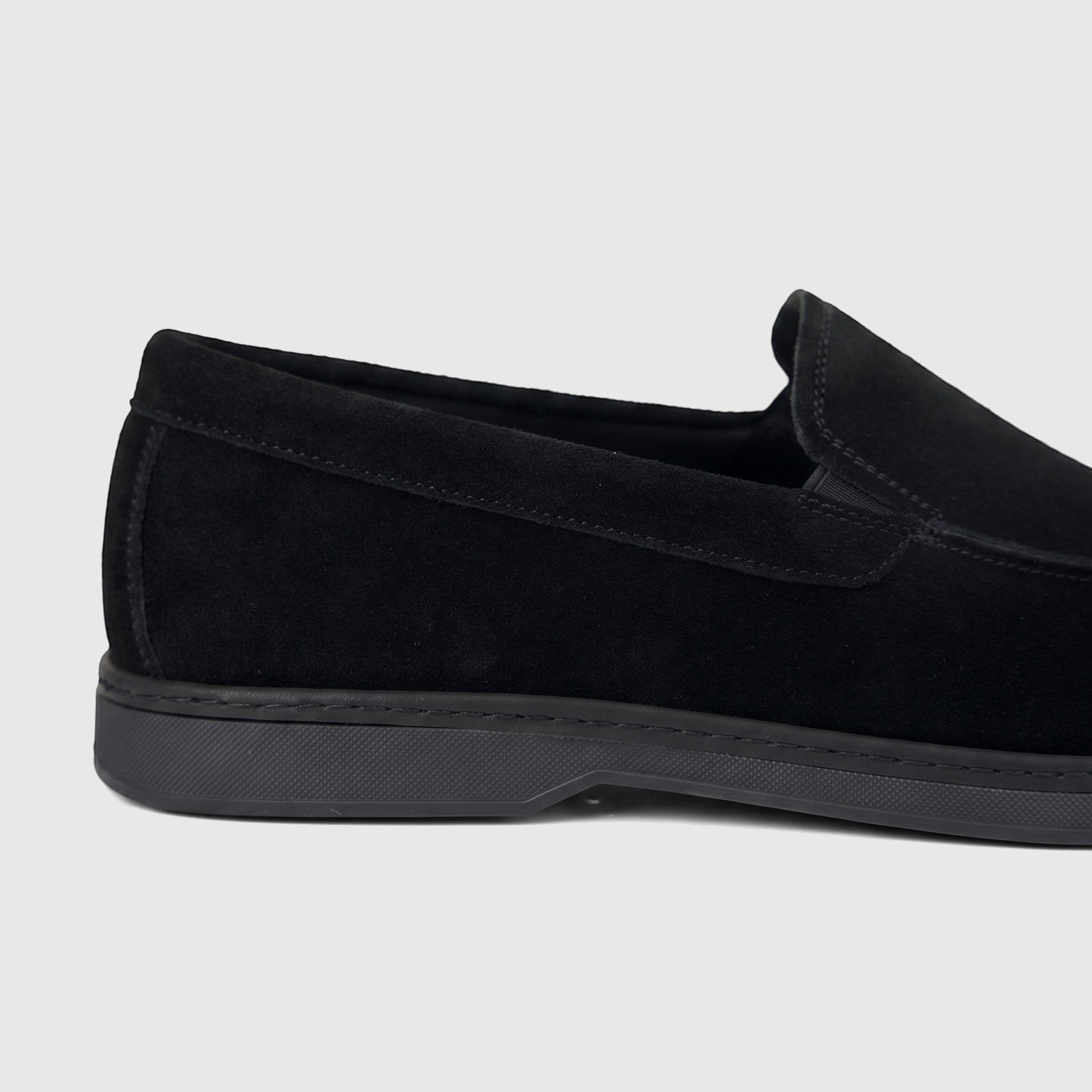 Close-up side view of a black suede Formales men's loafer, showcasing the stitching details and black sole.