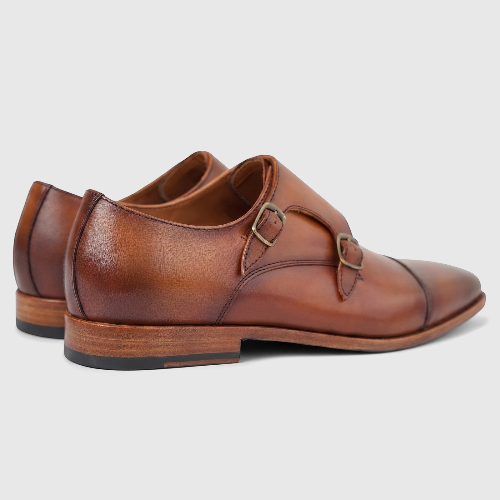 Brown leather double monk strap dress shoes for men, featuring brass buckles and a cap toe design, viewed from the side.