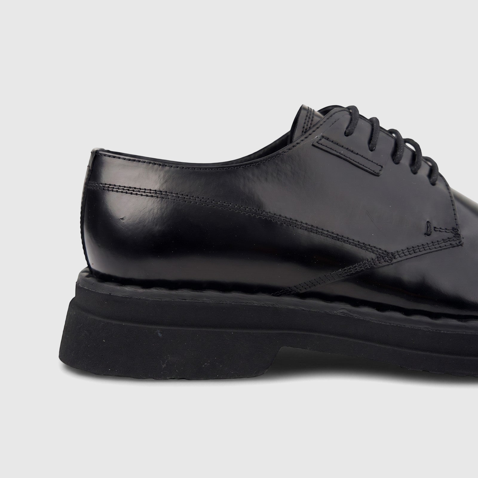 Close-up of a black patent leather men's formal shoe, featuring a hi-shine finish, chunky sole, and lace-up design.