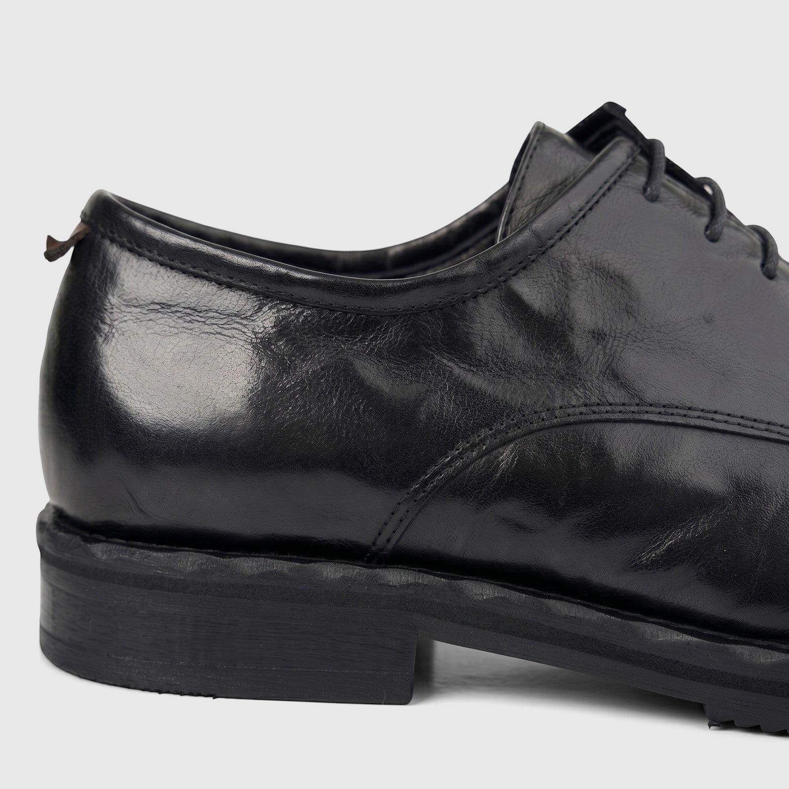Close-up of a black leather men's formal shoe with chunky sole and lace-up design, shown from the side.